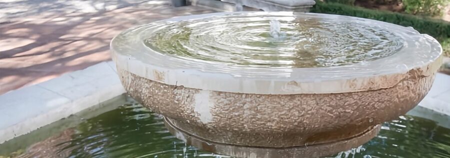 Fontana da giardino circolare in pietra con vasca colma d'acqua e piccolo zampillo centrale in funzione.