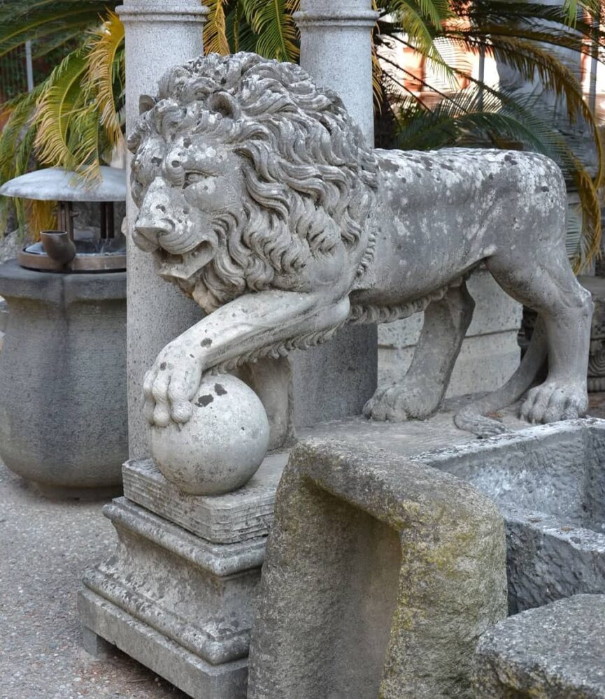 Statua decorativa da giardino in pietra raffigurante un leone con la zampa appoggiata su una sfera.