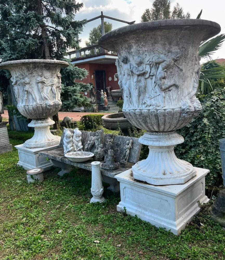 Coppia di grandi vasi da giardino in pietra decorati con rilievi di figure classiche su basi quadrate.